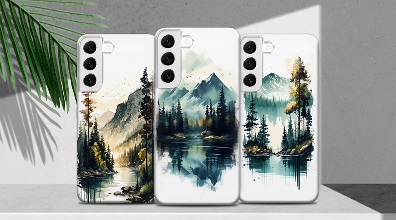 Puede incluir: Tres fundas para tel&eacute;fono con dise&ntilde;os de acuarela de un lago de monta&ntilde;a y un bosque. Las fundas son blancas con la parte posterior transparente y una protuberancia de c&aacute;mara negra.