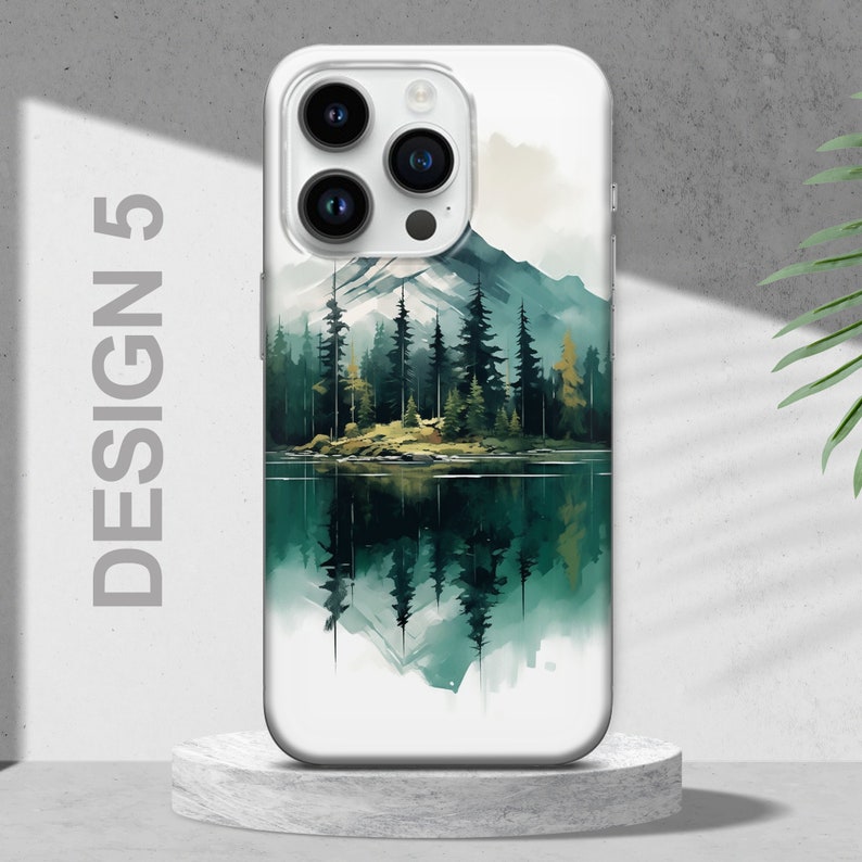 Puede incluir: Una funda de tel&eacute;fono blanca con un dise&ntilde;o de acuarela de un lago de monta&ntilde;a y un bosque. El dise&ntilde;o presenta un reflejo de los &aacute;rboles y las monta&ntilde;as en el agua.