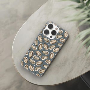 Op de afbeelding: Een transparante telefoonhoes met een blauwe achtergrond en een patroon van witte en bruine oesters. De hoes heeft een camera-uitsparing met drie zwarte cameralenzen.