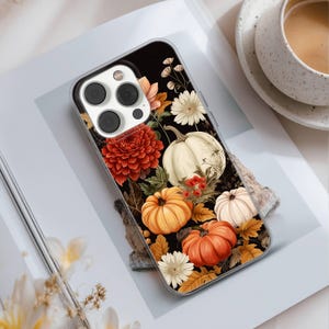 May include: A clear phone case featuring a fall-themed design. The case showcases a black background adorned with orange, white, and yellow pumpkins, flowers, and leaves. The design is a vibrant and colorful illustration, perfect for autumn.