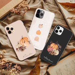 May include: Three phone cases with autumn-themed designs. One case is light pink with pumpkins and the name "Kamilla". Another is white with a mug, pumpkins, and a sweater. The third is black with pumpkins and the name "Adeline".