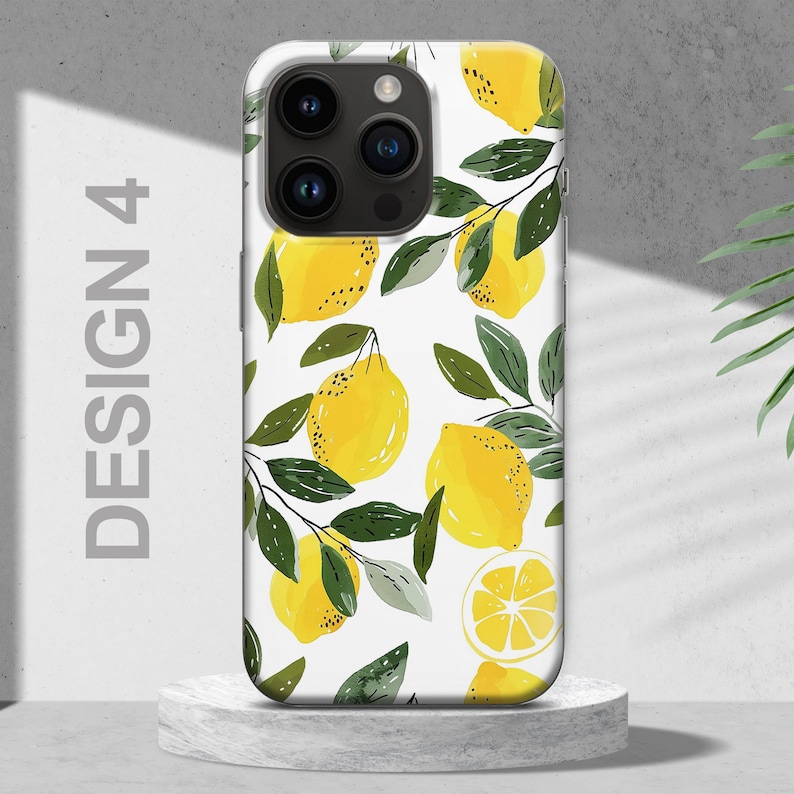 May include: White phone case with a design of yellow lemons and green leaves. The case has a camera lens cutout.
