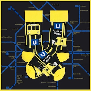 May include: A pair of yellow and black socks with a graphic print of the Berlin U-Bahn subway system. The socks feature a yellow train, a black U-Bahn logo, and the text "U-Bahn Berlin".