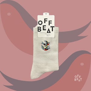 Op de afbeelding: Off-white geribbelde sokken met een kleurrijk geborduurd vogelontwerp. De sokken hebben een label met de tekst "OFF BEAT" en "offbeat-berlin.com". De sokken zijn maat 45-46 unisex.