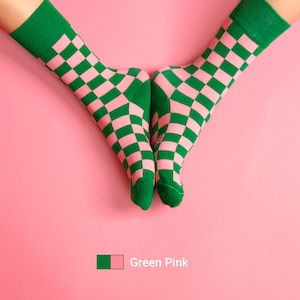May include: A pair of socks with a checkered pattern in green and pink. The socks are on a pink background.
