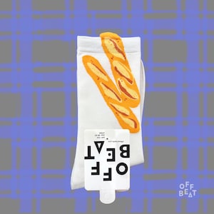 Pode incluir: Meias brancas com um desenho de duas baguetes laranja e amarelas. As meias têm o texto "OFF BEAT" numa etiqueta branca. Meias unissexo, tamanho 38-40.