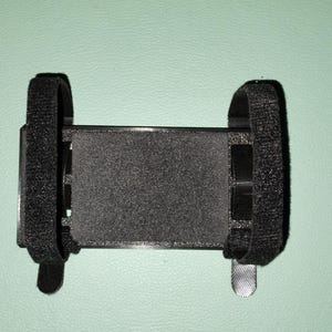 May include: Black adjustable phone holder with velcro straps. The holder is made of a soft, flexible material and can be used to secure a phone to a variety of surfaces.