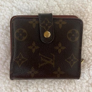 Könnte beinhalten: Braunes und beigefarbenes zweifach gefaltetes Portemonnaie mit goldfarbenem Druckknopfverschluss. Das Portemonnaie weist ein sich wiederholendes Muster aus ineinandergreifenden floralen und geometrischen Formen auf. Die Innenseite ist rotbraun.