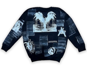 May include: Black long-sleeve sweatshirt with white graphic prints of an angel with wings, a face, a bird, and text that reads "UNLEASHING THE TRAGEDY WITHIN THE BOOK TO INSPIRE CREATIVITY."