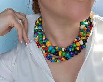 May include: A multi-strand necklace composed of colorful wooden beads in various sizes. The beads are in shades of blue, green, yellow, red, and white. The necklace is worn over a white collared shirt.