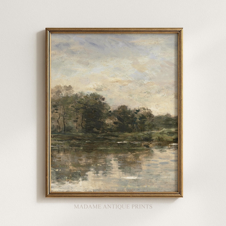 May include: A framed landscape painting featuring a calm body of water reflecting a cloudy sky and a line of dark green trees along the horizon. The artwork is enclosed in a thin, metallic gold frame and includes the text MADAME ANTIQUE PRINTS.