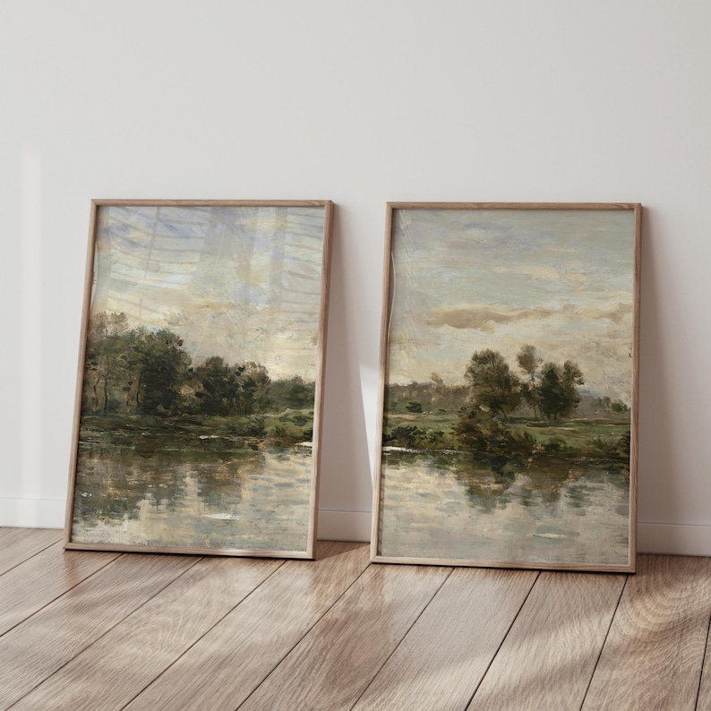 May include: Two vertical framed wall art prints featuring an impressionistic landscape painting of a calm river reflecting a line of dark green trees under a cloudy, muted sky with soft beige and grey tones, encased in light wood frames.
