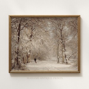 May include: A framed landscape painting depicting a snow-covered forest path with bare trees and a person walking a dog in the distance. The artwork features muted brown and white tones, encased in a thin metallic gold frame with the text MADAME ANTIQUE PRINTS.