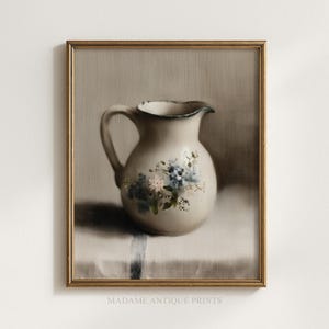 Op de afbeelding: Een ingelijst vintage stilleven schilderij van een crèmekleurige kan met een blauw bloemmotief. De kan heeft een donkerblauwe rand en een handvat. Het schilderij staat tegen een neutrale achtergrond. De tekst "MADAME ANTIQUE PRINTS" staat onderaan.