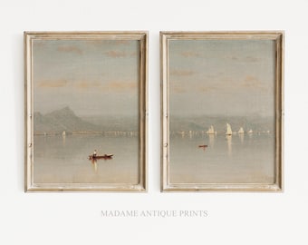 May include: Two framed landscape art prints featuring muted, soft-toned maritime scenes. Each print depicts a calm body of water with distant mountains, small sailboats, and a lone rowboat under a pale, hazy sky. The text MADAME ANTIQUE PRINTS appears below.