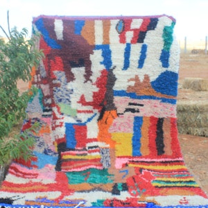 May include: A colorful Moroccan rug with a geometric pattern in shades of red, blue, yellow, green, and white. The rug is made of wool and has a fringe border.