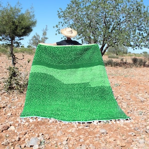 May include: A green and white woven rug with a textured surface. The rug is folded in half and held up by a person.