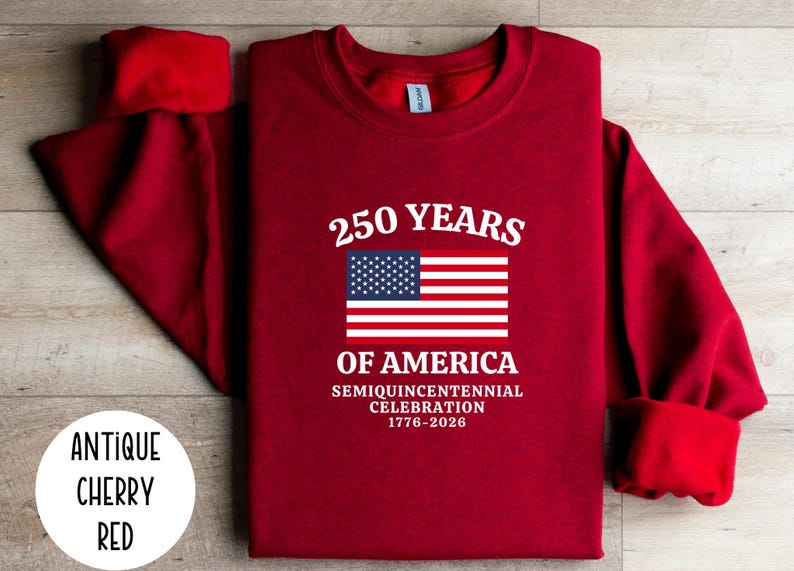 Puede incluir: Sudadera rojo cereza antiguo con el texto "250 YEARS OF AMERICA" y una bandera estadounidense. La sudadera celebra la Semiquincentennial Celebration de 1776-2026.