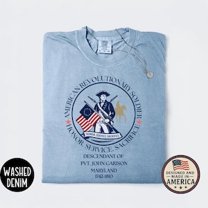 May include: Light blue Comfort Colors t-shirt with a circular graphic featuring an American Revolutionary soldier, the text "American Revolutionary Soldier", and the text "Honor, Service, Sacrifice". Includes the text "Descendant of Pvt. John Garison, Maryland 1742-1810".