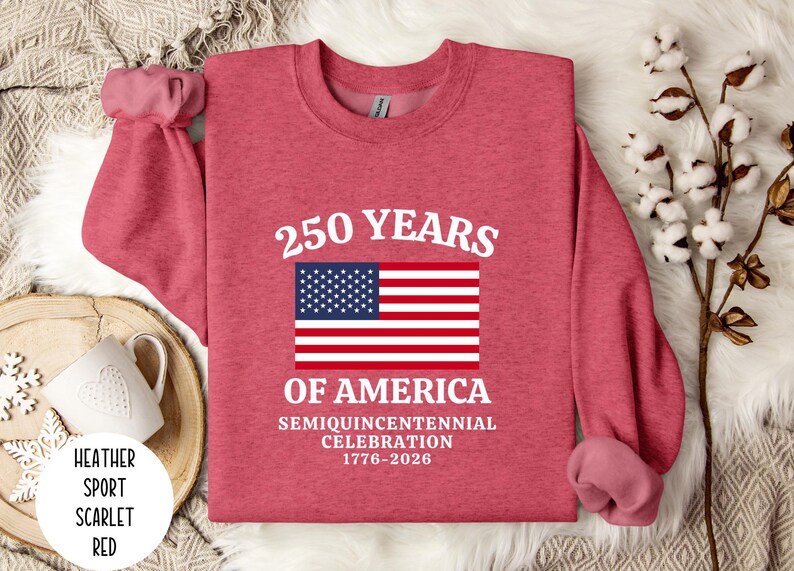 Puede incluir: Una sudadera roja escarlata con el texto "250 YEARS OF AMERICA" y una bandera estadounidense. La sudadera celebra el semiquincentenario de 1776-2026. La sudadera es de estilo deportivo jaspeado.
