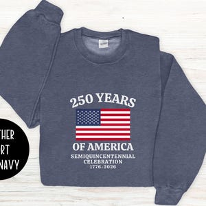 Puede incluir: Sudadera azul marino oscuro con el texto "250 YEARS OF AMERICA" y una bandera americana. La sudadera conmemora la celebraci&oacute;n del semiquincentenario de 1776-2026. La sudadera tambi&eacute;n tiene las palabras "Heather Sport Dark Navy" en un c&iacute;rculo negro.