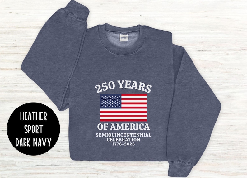 Puede incluir: Sudadera azul marino oscuro con el texto "250 YEARS OF AMERICA" y una bandera americana. La sudadera conmemora la celebraci&oacute;n del semiquincentenario de 1776-2026. La sudadera tambi&eacute;n tiene las palabras "Heather Sport Dark Navy" en un c&iacute;rculo negro.