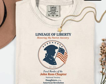May include: Ivory-colored t-shirt with the text "LINEAGE OF LIBERTY" and a patriotic graphic. The graphic includes a silhouette of a person holding a flag, surrounded by stars and the text "John Ross Chapter".