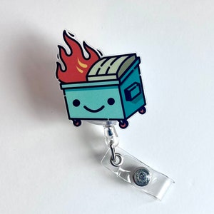 May include: A blue and green cartoon bin with a smiling face and flames on top. The bin is attached to a clear plastic retractable badge holder.