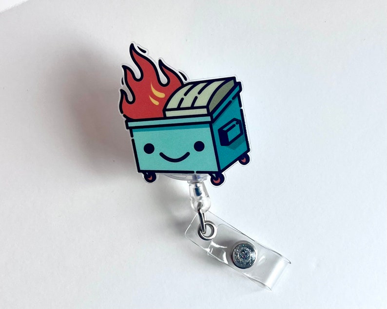 May include: A blue and green cartoon bin with a smiling face and flames on top. The bin is attached to a clear plastic retractable badge holder.
