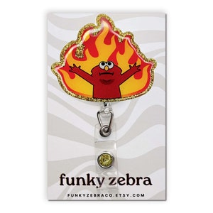 May include: A red Sesame Street character with a yellow flame design, on a gold glitter background, attached to a clear retractable badge holder with a gold glitter button. The text "funky zebra" and "FUNKYZEBRACO.ETSY.COM" is printed on the card.