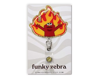 Op de afbeelding: Een rood Sesamstraat-personage met een geel vlamontwerp, op een gouden glitterachtergrond, bevestigd aan een transparante intrekbare badgehouder met een gouden glitterknop. De tekst "funky zebra" en "FUNKYZEBRACO.ETSY.COM" staat op de kaart gedrukt.