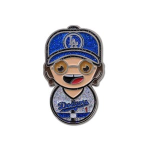 May include: A glittery enamel pin depicting a cartoon character in a blue Dodgers baseball cap and jersey. The pin shows a smiling face with glasses and the Dodgers logo. The jersey has the word "Dodgers" and the number "1".