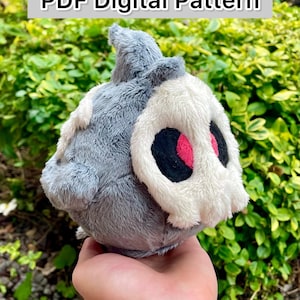 May include: A plush toy in the shape of a skull with a gray body and a white skull face. The eyes are black with pink accents. The text "PDF Digital Pattern" is at the top.