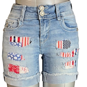 Op de afbeelding: Lichtblauwe denim shorts met distressed patches met rood, wit en blauw patriottisch patroon. De shorts hebben een klassiek vijf-zakken ontwerp, een knoop- en ritssluiting en opgerolde manchetten. De shorts zijn ontworpen met een hoge taille.