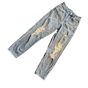 May include: Light blue denim jeans with distressed detailing. The jeans feature multiple rips and tears across the front of the legs. The jeans have a classic five-pocket design and a button and zip closure.