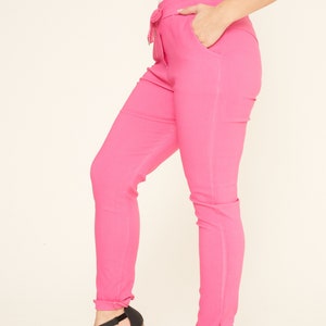 Puede incluir: Pantalón pitillo rosa con cintura de cordón y dobladillo vuelto. El pantalón se combina con sandalias de tacón negras.