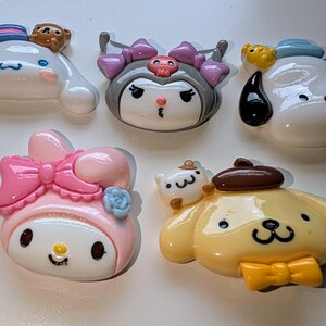 May include: Six colorful cartoon character charms, including a pink Hello Kitty, a yellow dog with a brown hat, a white dog with a blue hat, a black and white character with a purple hat, and two smaller white characters.