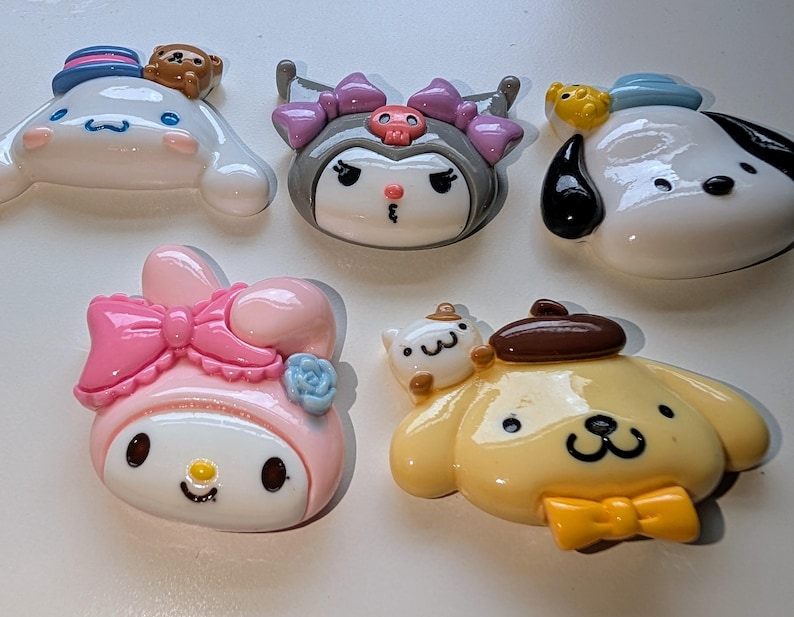 May include: Six colorful cartoon character charms, including a pink Hello Kitty, a yellow dog with a brown hat, a white dog with a blue hat, a black and white character with a purple hat, and two smaller white characters.