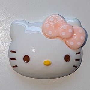 May include: White ceramic figurine of Hello Kitty with a pink bow with white polka dots.