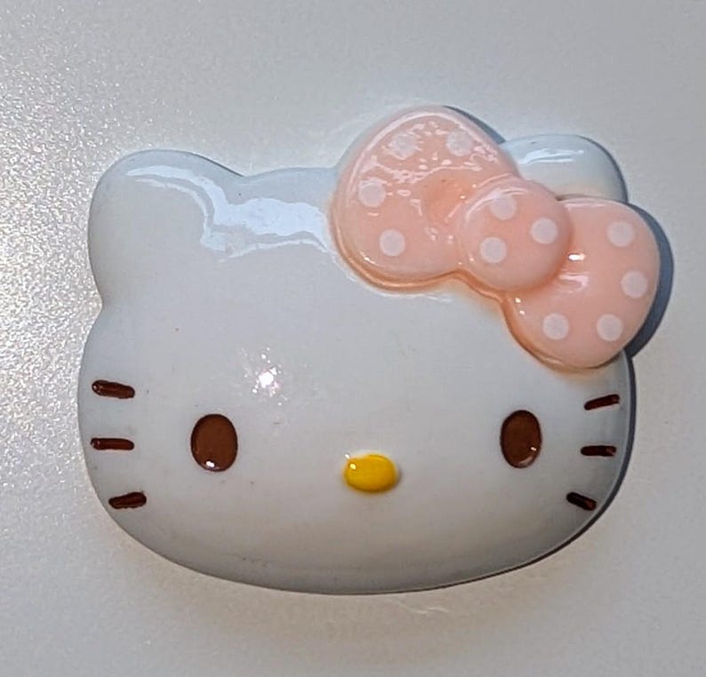 May include: White ceramic figurine of Hello Kitty with a pink bow with white polka dots.