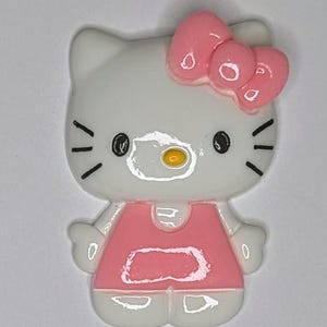 May include: A white and pink Hello Kitty figurine with a pink bow on her head. She is wearing a pink dress and has black eyes and a yellow nose.