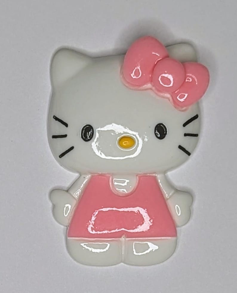 May include: A white and pink Hello Kitty figurine with a pink bow on her head. She is wearing a pink dress and has black eyes and a yellow nose.