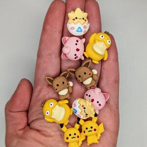 Puede incluir: Una colecci&oacute;n de figuras de personajes de dibujos animados coloridos, incluyendo Pikachu, Eevee y otros, en varias poses. Las figuras son peque&ntilde;as y detalladas, con colores brillantes y rasgos distintivos. Los personajes se sostienen en una mano.