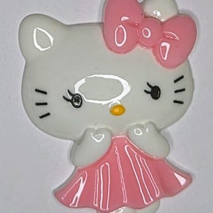 May include: A white ceramic figurine of a cartoon cat wearing a pink dress and a pink bow. The cat has black eyes and a yellow nose.