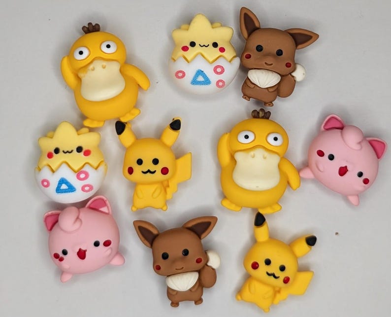 Puede incluir: Una colecci&oacute;n de figuras de personajes coloridos, incluyendo patos amarillos, Pikachu, Eevee marr&oacute;n y Jigglypuff rosa. Las figuras tienen detalles y est&aacute;n dispuestas sobre un fondo claro. Probablemente sean objetos de colecci&oacute;n.