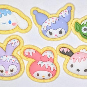 May include: Six colorful cartoon character iron-on patches with a yellow waffle-like border. The characters include a purple bunny, a pink bunny, a white dog, a blue character with horns, a green alien, and a white dog with a pink bow.