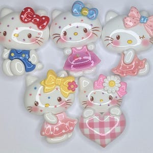 Puede incluir: Cinco figuritas de cerámica blanca Hello Kitty con lazos y vestidos de diferentes colores. Las figuritas llevan todas atuendos diferentes, incluyendo un mono azul, un vestido rosa, un vestido rosa con lunares blancos, un vestido rosa con cuadros blancos y un vestido rosa con lunares blancos.
