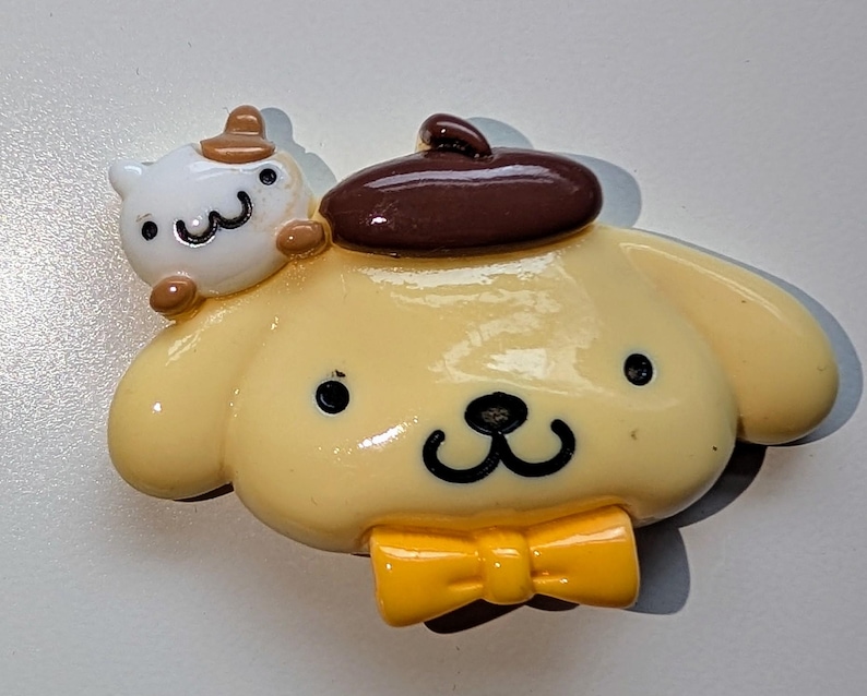 May include: A yellow and brown cartoon dog figurine wearing a brown hat and a yellow bow tie. The dog has a small white cat figurine on its back.