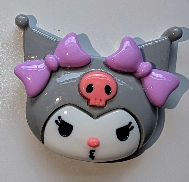May include: A gray and white character with pink bows and a pink skull on its head. The character has large eyes and a small pink nose.