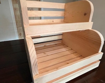 May include: A two-tiered wooden storage shelf. The shelf is constructed from light-colored wood and features a slatted design for both the base and the back. The sides have curved supports, and the overall design is rustic and functional.